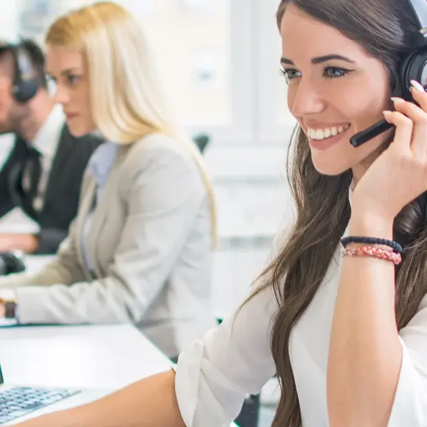 Eine Frau mit Headset sitzt am Rechner und telefoniert freundlich lächelnd. 